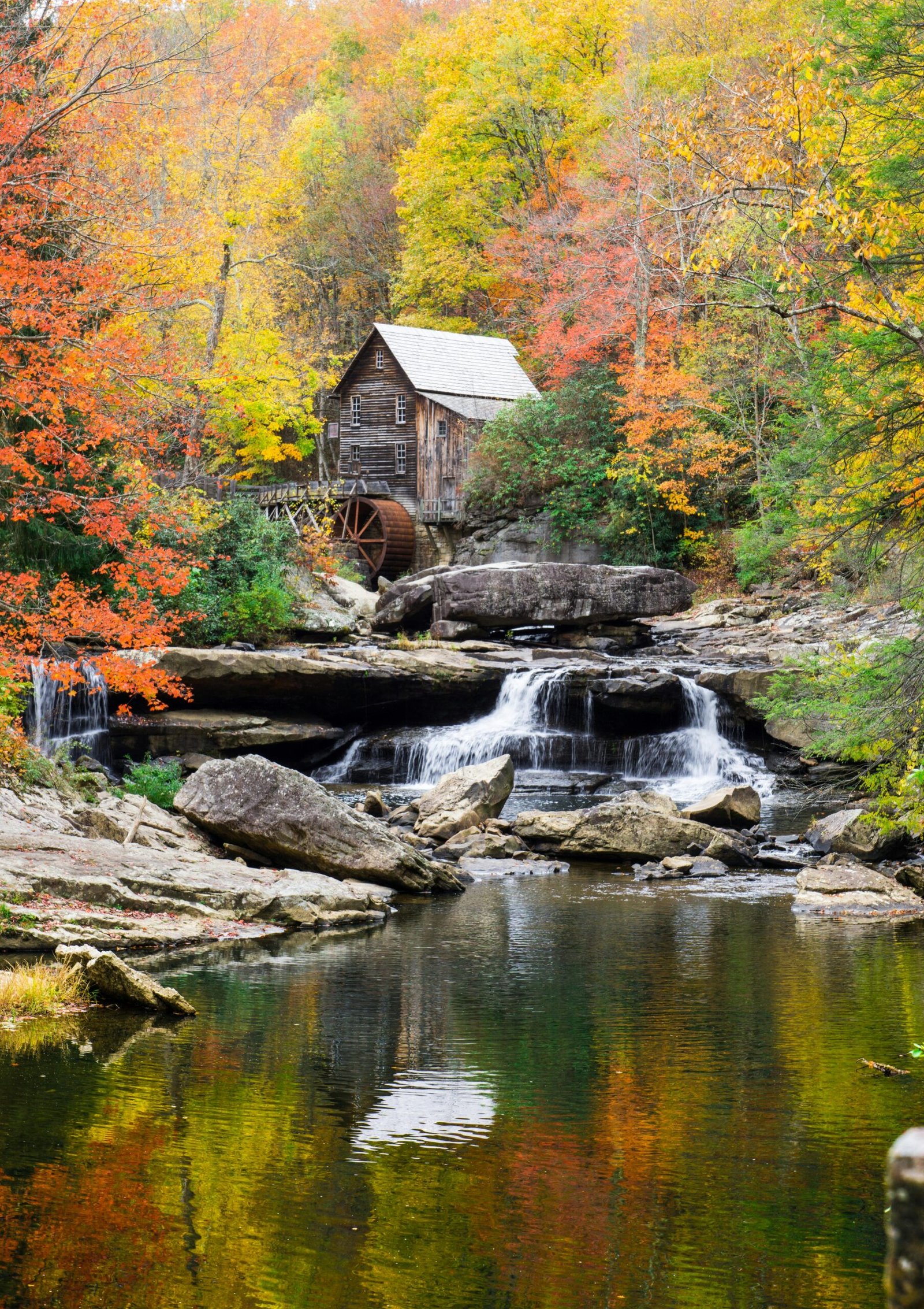 Idyllic scene of a gristmill surrounded by colorful autumn trees, reflecting in a serene creek.
